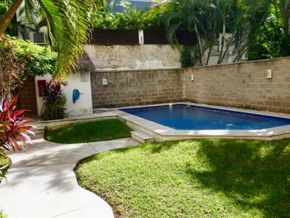 Condo for sale in downtown Cancún – rectangular pool in backyard surrounded by a tropical garden and a stone wall