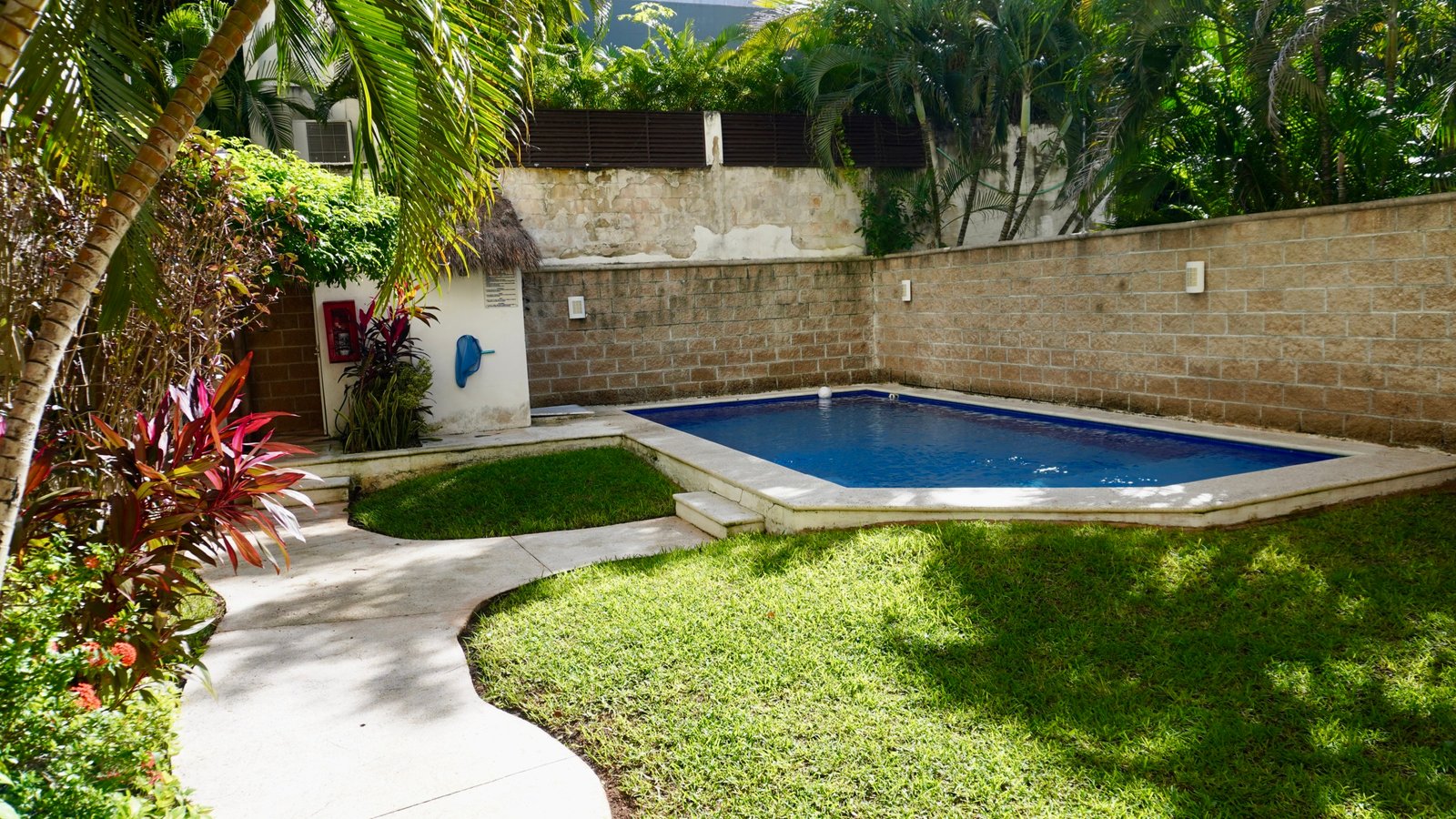 Condo for sale in downtown Cancún – rectangular pool in backyard surrounded by a tropical garden and a stone wall