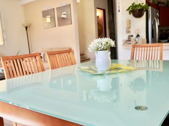 Apartment for sale in downtown Cancun – Dining room with glass table and wooden chairs. At the back, a living room