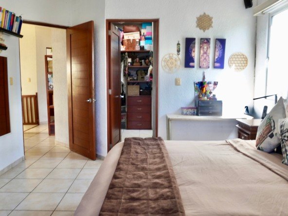 Apartment for sale in downtown Cancun – Bedroom with a large bed and traditional wooden furniture. A walk-in closet is visible.